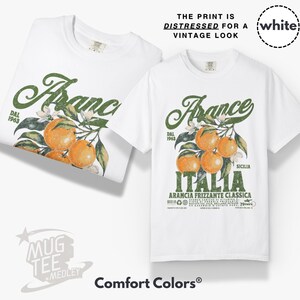 May include: Two white t-shirts with a distressed vintage print. The design features the word "Arance" in green script, oranges, and the word "ITALIA". The text "THE PRINT IS DISTRESSED FOR A VINTAGE LOOK" is at the top.
