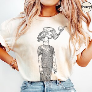 Comfort Colors® ivory unisex T-shirt featuring Prakash’s hand-drawn line-art figure; close-up on model with rolled sleeves to highlight the black front print and soft cotton texture.
