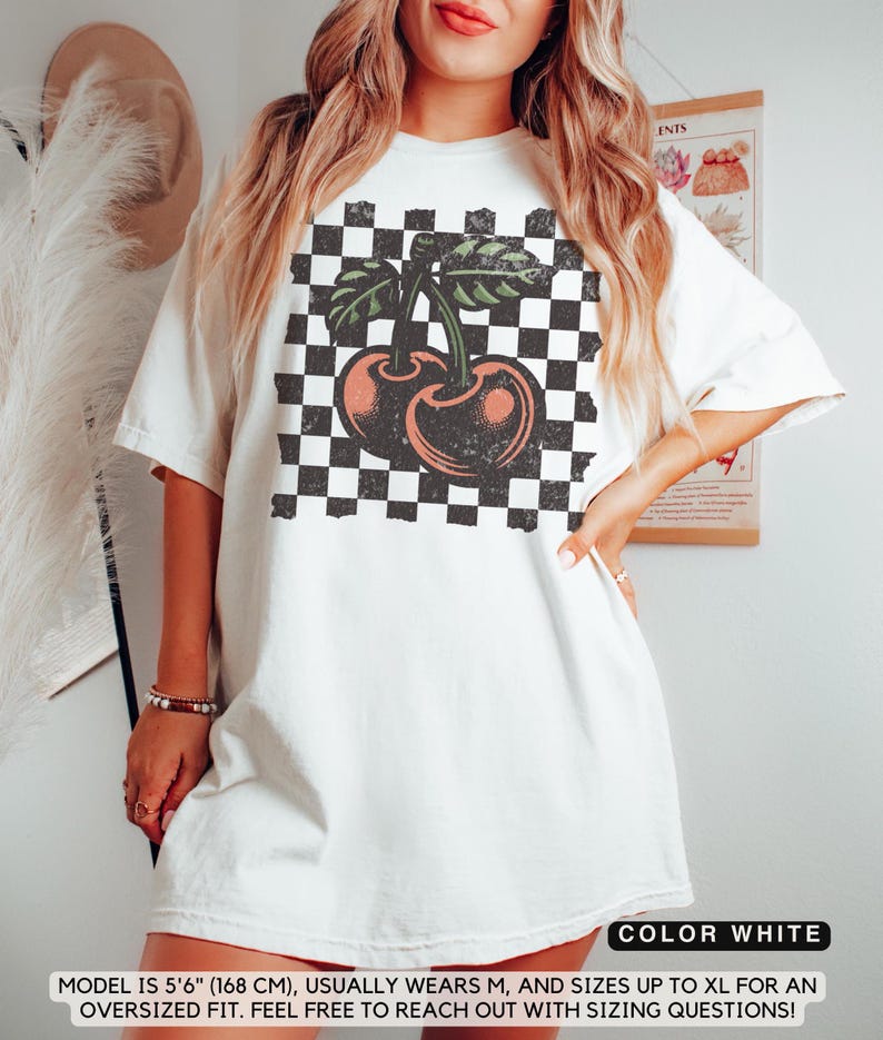 May include: White oversized t-shirt with a black and white checkered pattern and a vintage-style cherry graphic. The model is 5'6" (168 cm) and usually wears a size M.  The shirt is available in sizes up to XL.