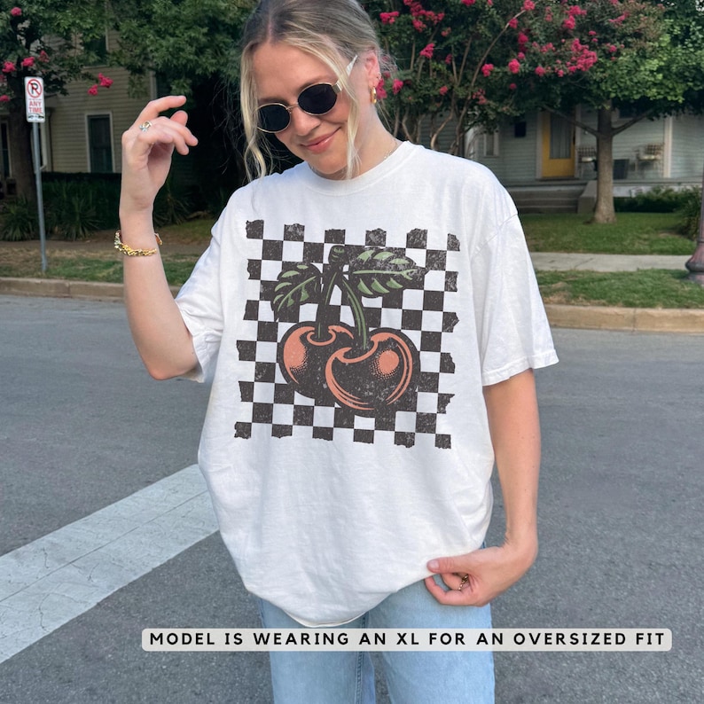 Female model wearing a white Comfort Colors checkered cherries t-shirt – vintage distressed streetwear tee with retro 90s Y2K aesthetic.