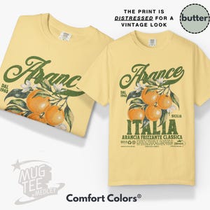 May include: Two light yellow t-shirts with a vintage-style graphic. The design features the word "France" in green script, oranges, and the word "Italia". The text "The print is distressed for a vintage look" is also visible.