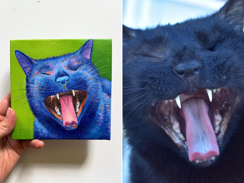 May include: A vibrant painting of a blue cat yawning, set against a green background. The cat's mouth is wide open, revealing its pink tongue and sharp teeth. The artwork is held by a person's hand, showcasing the canvas's square shape.