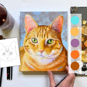 May include: A vibrant painting of a ginger tabby cat with green eyes. The artwork is on a small canvas, with a color palette guide and paintbrushes nearby. The cat's fur is detailed with orange and brown stripes, set against a blue background.