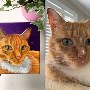 May include: A square canvas painting of an orange tabby cat with green eyes and a white chest, set against a purple background. The painting is held up next to a real orange tabby cat with green eyes.