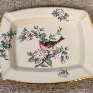 May include: Cream-colored rectangular dish with a gold rim, featuring a bird perched on a flowering branch. The bird has a pink breast and brown wings. Pink and white flowers and green leaves decorate the dish.