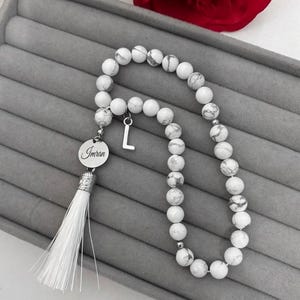 K&ouml;nnte beinhalten: Wei&szlig;e Gebetsperlen mit einem wei&szlig;en Quasten und einem silbernen Anh&auml;nger mit dem Namen "Imran" und dem eingravierten Buchstaben "L".
