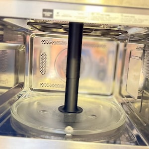 Può includere: Vista interna di un forno a microonde in acciaio inossidabile. Un piatto di vetro trasparente si trova sul fondo, con un meccanismo rotante nero al centro. Le pareti interne sono metalliche e la porta è aperta.
