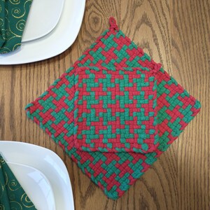 May include: Two red and green woven pot holders, one on top of the other. The pot holders are made of a thick, woven material and have a square shape.