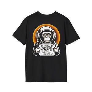 Può includere: T-shirt nera con grafica di uno scimpanzé con casco da astronauta su un cerchio arancione. Lo scimpanzé tiene in mano un cartello con la scritta: "IN A WORLD OF PROPAGANDA, THE TRUTH IS ALWAYS A CONSPIRACY."