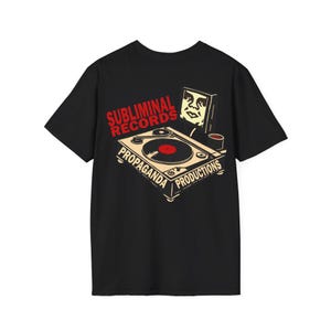 May include: Black t-shirt featuring a graphic design with a turntable, a portrait, and the text "Subliminal Records" and "Propaganda Productions" in red and beige. The turntable has a red record.