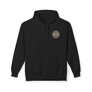 May include: Black hooded sweatshirt with a front pocket and a drawstring hood. The sweatshirt features a circular emblem on the upper left chest with a geometric design in shades of brown and tan.