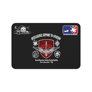 Könnte beinhalten: Eine rechteckige schwarze Schreibtischunterlage mit dem Abzeichen des 160th Special Operations Aviation Regiment. Das Design zeigt einen roten Schild mit Schwert, Flügeln, dem Text Intelligence Support to Aviation und einem Logo mit Hubschrauber.