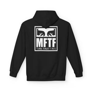 Può includere: Felpa con cappuccio nera con grafica bianca sul retro. La grafica presenta occhi stilizzati sopra le lettere "MFTF" e il testo "TASK FORCE 1-160" all'interno di un rettangolo bianco.