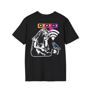 Pode incluir: Camiseta preta com um gráfico branco que retrata uma pessoa sentada com um telefone, um pássaro azul e ícones de mídia social. O design inclui um símbolo wi-fi e um ícone de coração no telefone.