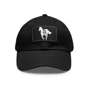 Könnte beinhalten: Schwarze Baseballkappe mit gebogenem Schirm. Ein weißes rechteckiges Patch auf der Vorderseite zeigt eine laufende Pferdesilhouette mit dem Buchstaben "D" darin. Die Kappe ist aus einem weichen, strapazierfähigen Stoff gefertigt.