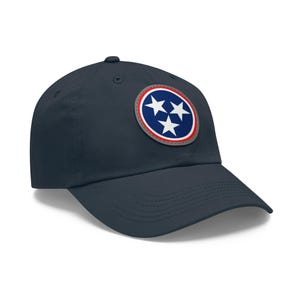 May include: Navy blue baseball cap featuring a circular patch with three white stars on a blue background, encircled by red and white borders. The cap has a curved brim and a button on top, offering a classic, casual style.