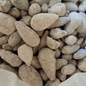 May include: A close-up of a pile of small, light gray, irregularly shaped stones. The stones are smooth and have a slightly rough texture.