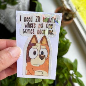 May include: A sticker featuring a cartoon dog with a sad expression. The sticker has a holographic finish and says "I need 20 minutes where no one comes near me."