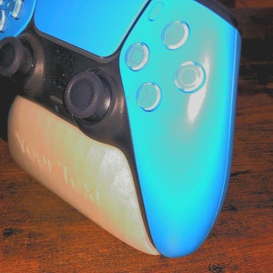 Könnte beinhalten: Ein blauer Videospiel-Controller mit schwarzen Knöpfen und einem weißen Ständer. Der Ständer hat den Text "Your Text" aufgedruckt.