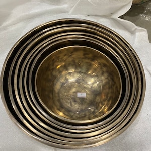 Może przedstawiać: Zestaw siedmiu gniazdowych misek mosiężnych, każda z młotkowanym wykończeniem. Miski są ułożone w okrągły wzór, z największą miską na dole i najmniejszą na górze. Wszystkie miski są wykonane z tego samego materiału i mają podobny design.