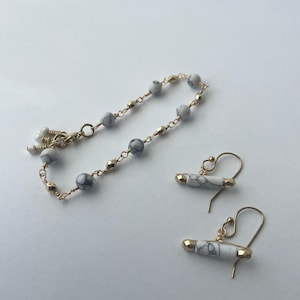 May include: A set of white and gold jewelry featuring a bracelet with white marble beads and gold accents and a pair of earrings with white marble beads and gold accents.