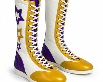 May include: A pair of tall, lace-up wrestling boots featuring a white base with gold and purple accents. The boots have white laces, a gold toe cap, and a purple heel panel. The side of the boot is decorated with three star-shaped appliques.