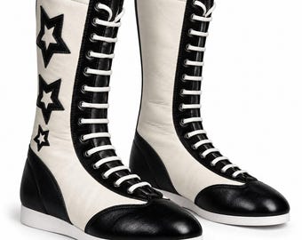 May include: A pair of mid-calf boots featuring a black and white color scheme. The boots have white laces, black toe caps, and black heel counters. The outer side of the left boot is decorated with three black star appliques of varying sizes.