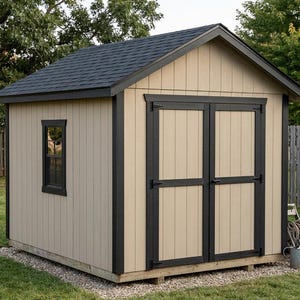 May include: A tan wooden shed with a black shingled roof, black trim, and double doors. The shed has a small window and is set on a gravel base in a grassy yard. A garden hose and watering can are visible.