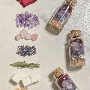 Puede incluir: Tres pequeñas botellas de vidrio llenas de varios cristales, lavanda seca, pétalos de rosa y sal rosa del Himalaya. Las botellas tienen tapones de corcho. Las botellas están dispuestas sobre una superficie blanca con otros cristales, lavanda seca, pétalos de rosa y cubos de azúcar.
