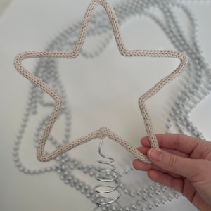 May include: A beige knitted star tree topper with a silver metal spring attached to the bottom.