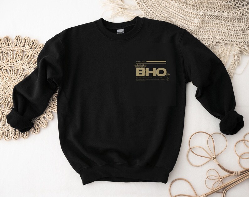 Op de afbeelding: Zwart sweatshirt met een gouden kroon en de tekst "BHO" bedrukt op de voorkant.