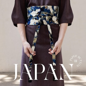 May include: A dark brown kimono with a blue and white crane obi belt. The obi belt has a detailed pattern of white cranes and gold accents. The word "JAPAN" is displayed in large white letters at the bottom of the image.