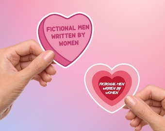 Könnte beinhalten: Zwei rosa herzförmige Aufkleber mit dem Text "Fictional Men Written By Women" darauf. Die Aufkleber werden von zwei Händen gehalten.
