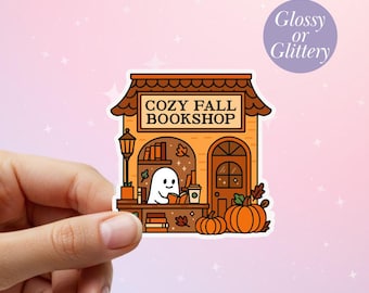 May include: A sticker featuring a cozy fall bookshop illustration. The shop has an orange facade, a brown roof, and a ghost reading a book. Pumpkins and fall leaves decorate the scene. The text "COZY FALL BOOKSHOP" is displayed.