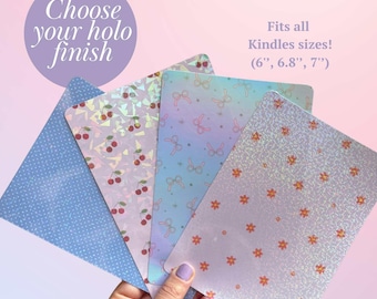 Pode incluir: Cinco skins de vinil holográfico diferentes para leitores eletrônicos Kindle. As skins apresentam vários padrões, incluindo cerejas, laços e flores. O texto "Choose your holo finish" e "Fits all Kindles sizes! (6", 6.8", 7")" é visível na imagem.