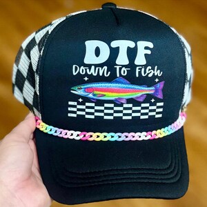 May include: A black trucker hat with a white and black checkered mesh back. The front features the text DTF Down To Fish in white, a colorful rainbow trout graphic, a white checkered pattern, and a pastel rainbow-colored plastic chain trim.
