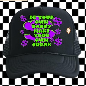 May include: Black trucker hat with a curved brim and mesh back. The front features the text "BE YOUR OWN DADDY MAKE YOUR OWN SUGAR" in green and purple, with dollar sign graphics. A small logo is on the side.