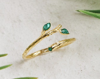 May include: Gold ring with a twig design and three green leaves. The ring is made to look like a branch with leaves.
