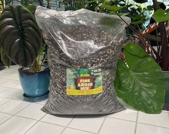May include: A bag of Fine Aroid Mix potting soil for plants. The bag is clear plastic and shows the soil inside. The soil is a dark brown color with white perlite mixed in. The bag has a yellow label with the words "Fine Aroid Mix" in black text. The label also has a picture of a plant.