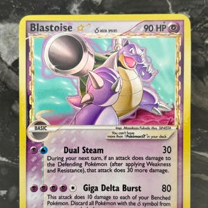 Puede incluir: Una carta coleccionable de Pokémon con Blastoise, una criatura parecida a una tortuga de color púrpura y marrón. La tarjeta tiene un borde amarillo e incluye texto como "Dual Steam" y "Giga Delta Burst". La tarjeta está etiquetada como "2024/NON-OFFICIAL CARD".