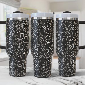 May include: Three black stainless steel travel mugs with a white ghost pattern. The mugs have a lid and a handle.