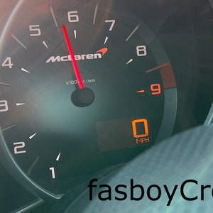 May include: A close-up of a car's dashboard with a speedometer reading 0 mph. The tachometer is a McLaren brand and reads 6,000 rpm. The temperature is 69 degrees Fahrenheit and the range is 60 miles.
