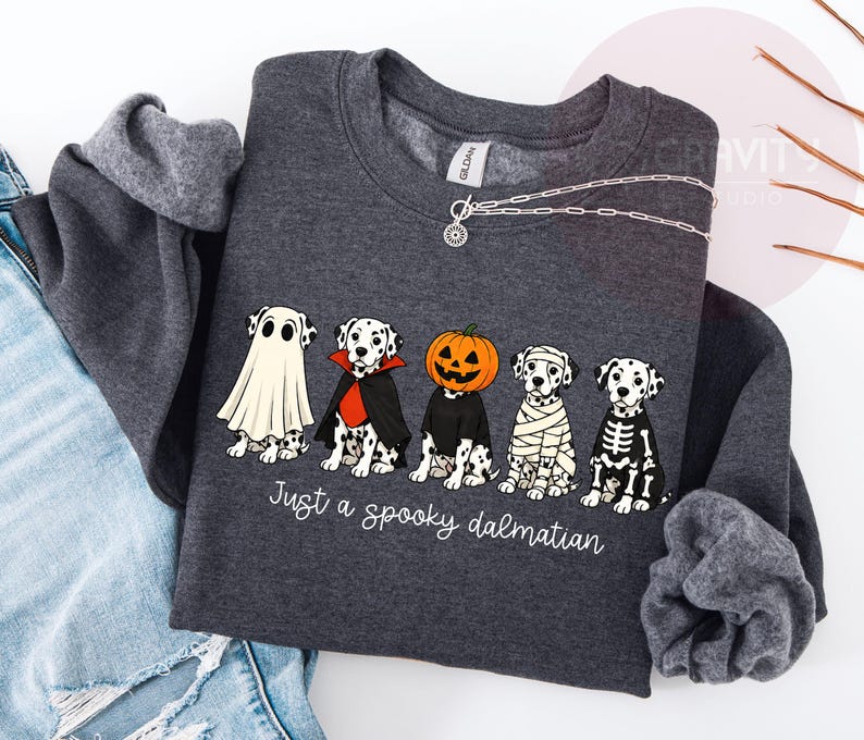 May include: A dark gray crewneck sweatshirt featuring a graphic of five Dalmatian dogs in Halloween costumes, including a ghost, vampire, pumpkin head, mummy, and skeleton. The text below the dogs reads, Just a spooky dalmatian.
