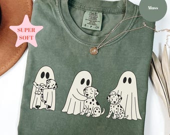May include: A moss green short-sleeve t-shirt featuring a graphic of three white ghosts interacting with spotted dalmatian puppies. The shirt has a crew neckline and a Comfort Colors brand label printed on the inside of the collar area.