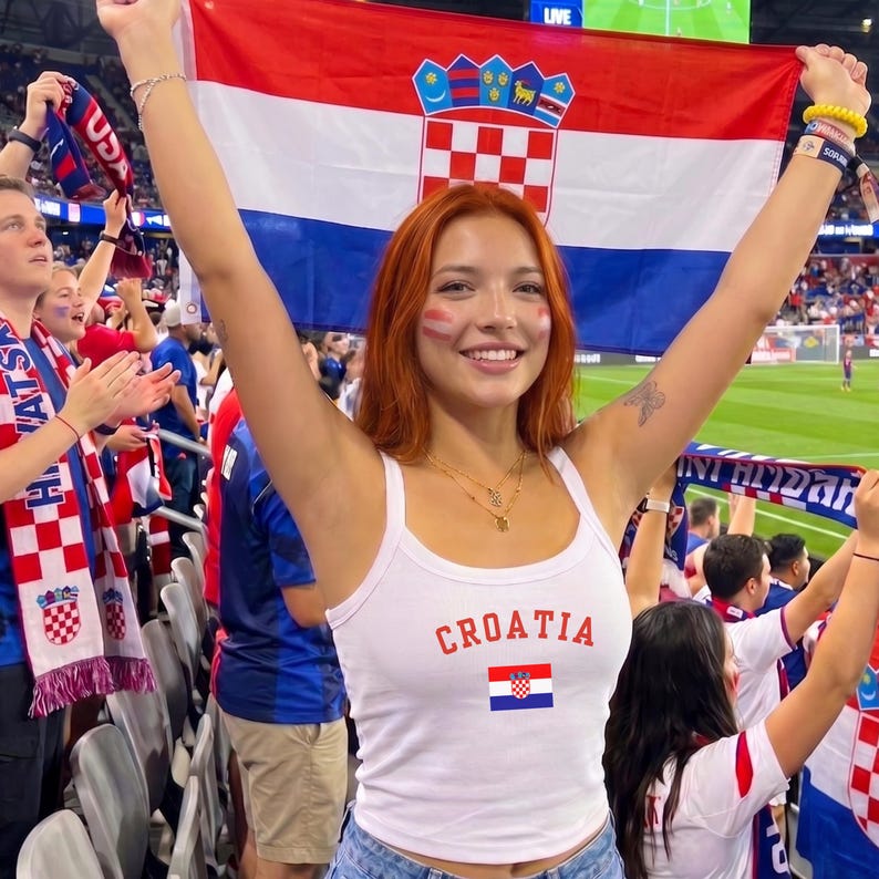 May include: A white tank top featuring the word CROATIA in red letters above a small Croatian flag graphic. The garment is worn by a person with red hair who is holding a large Croatian flag with red, white, and blue horizontal stripes.