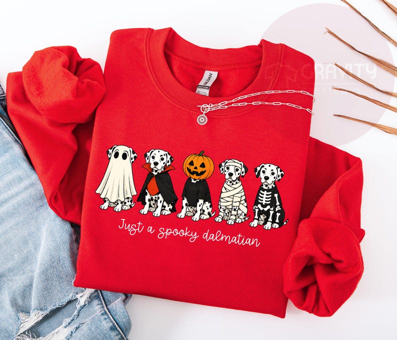 May include: A bright red crewneck sweatshirt featuring a graphic of five Dalmatian dogs in various Halloween costumes, including a ghost, vampire, pumpkin head, mummy, and skeleton. The text below the dogs reads Just a spooky dalmatian.