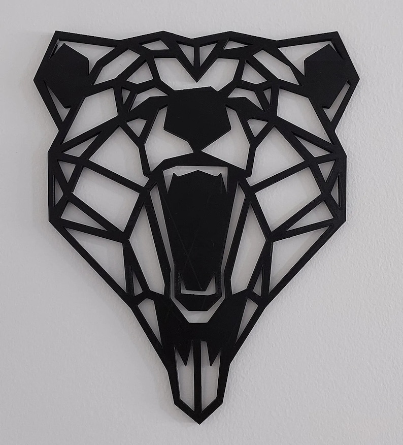 May include: Black geometric bear head wall decor. The bear's mouth is open and its teeth are visible. The bear's eyes are also visible.