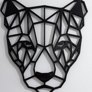 May include: Black geometric animal head wall decor. The head is made of wood and is shaped like a panther. The design is modern and minimalist.
