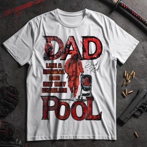 Può includere: T-shirt bianca con un design grafico rosso e nero. Il design include il testo "DAD" e "POOL", oltre a un'illustrazione di un personaggio in tuta rossa che spinge un passeggino. Il testo recita "Like a normal dad but way deadlier".
