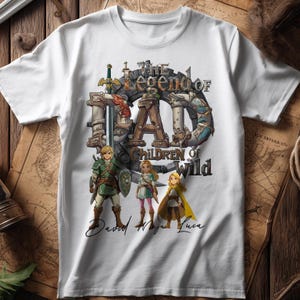 Könnte beinhalten: Weißes T-Shirt mit einem grafischen Design. Das Design enthält den Text "The Legend of Dad" und "Children of the Wild" sowie Illustrationen von Videospielcharakteren. Die Namen "David", "Maya" und "Luca" sind darunter geschrieben.